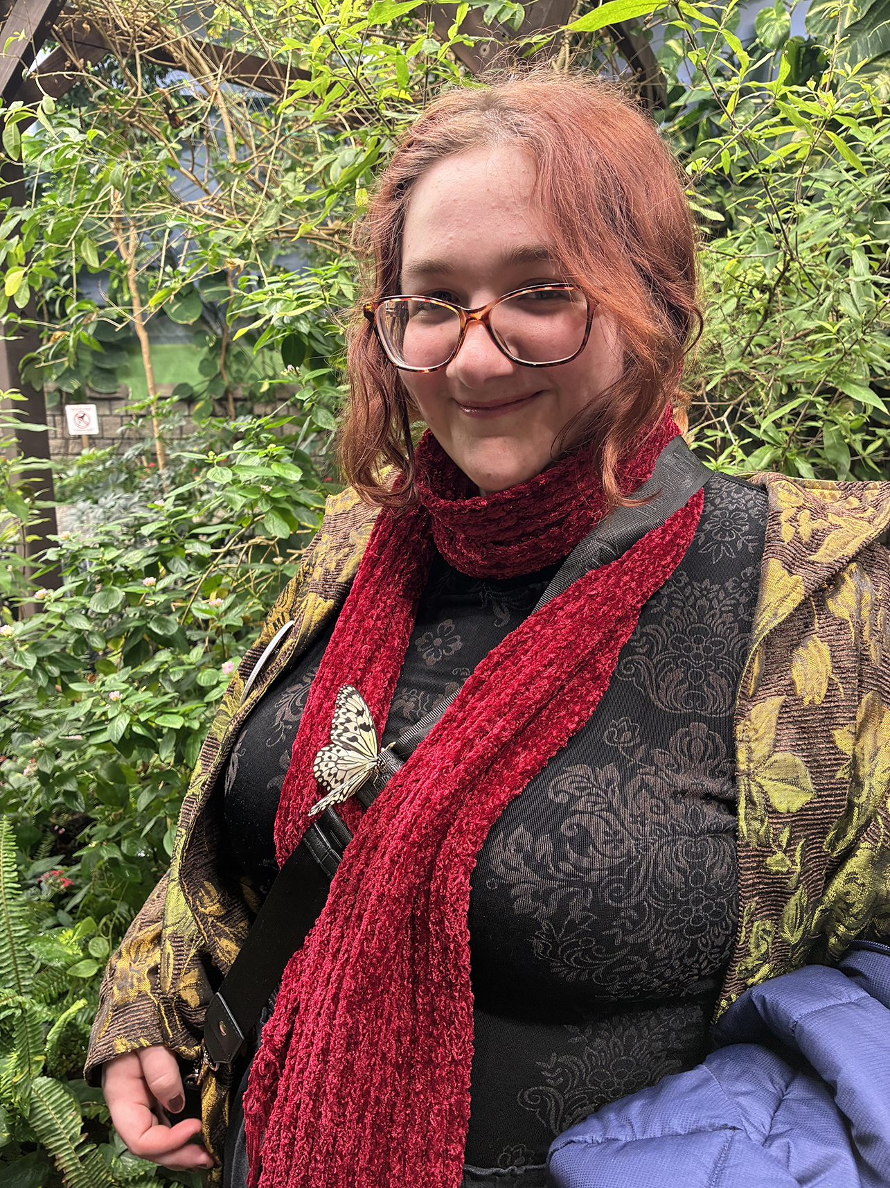 Young person with glasses, red scarf and butterfly brooch.